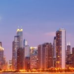 A city skyline with buildings lit up at night.